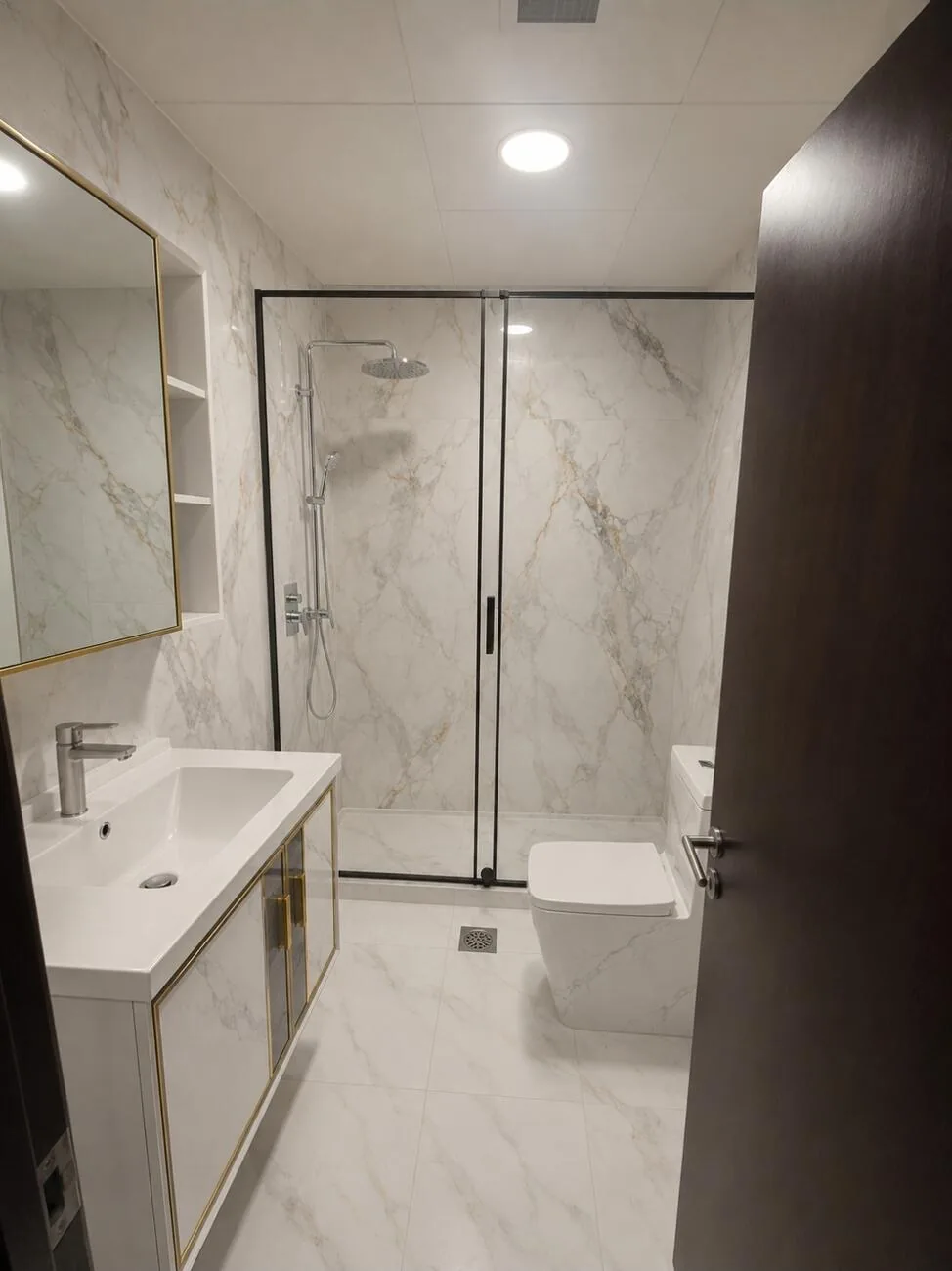 Bathroom after — marble walk-in shower with brushed-gold vanity